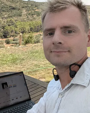 Henry working on a laptop outdoors, hills behind him